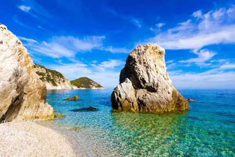 Scogliera imponente su una spiaggia di ciottoli, mare cristallino e isole verdi all'orizzonte. Una splendida località di mare tra Lazio e Toscana.