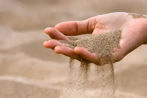 Mano che lascia cadere sabbia bianca, come il tempo che scorre via.