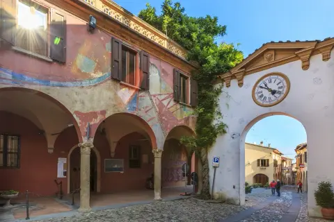 Un arco con orologio conduce a una strada acciottolata, un invito a scoprire i borghi da visitare vicino a Forlì.