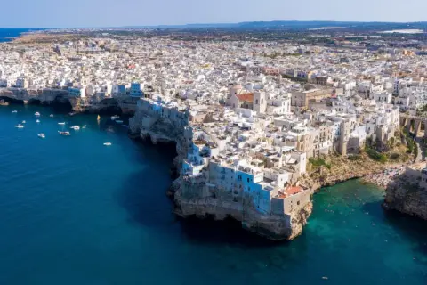Vista aerea di Polignano a Mare, con le case bianche a picco sul mare blu intenso. Un gioiello della Valle d'Itria, dove il mare incontra la terra.
