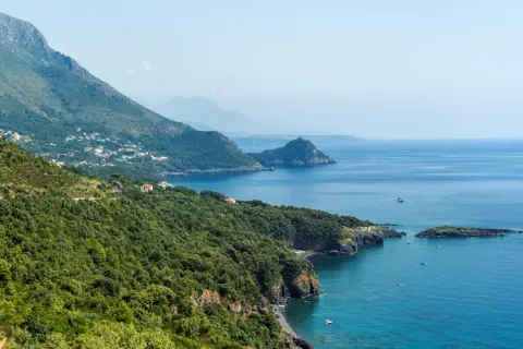 Costa verde e blu intenso del policastro mare, con case sparse tra la vegetazione e montagne sullo sfondo.