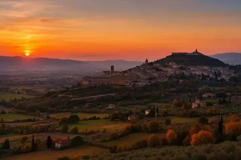 Tramonto infuocato su una città dell'Umbria arroccata su una collina, con uliveti e campi dorati.