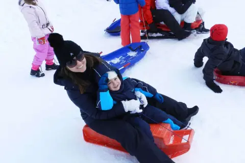 Mamma e bambino felici sciano in Abruzzo con slittino. Altri bambini giocano sulla neve.