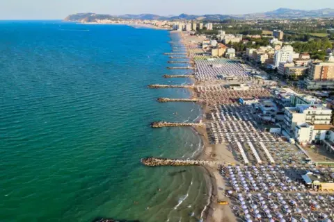 Vista aerea di una spiaggia affollata con ombrelloni colorati e il mare azzurro, tipica di una città riviera romagnola.