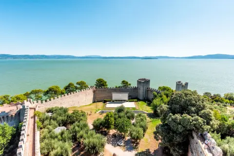 Vista dall'alto di un castello con un cinema all'aperto, circondato da ulivi e affacciato sul lago Trasimeno, uno dei borghi vicino Castiglione del Lago.