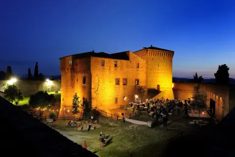 Rocca Malatestiana illuminata di sera, con persone che socializzano e godono dell'atmosfera. Un luogo suggestivo da scoprire tra le cose da vedere a Cesena.