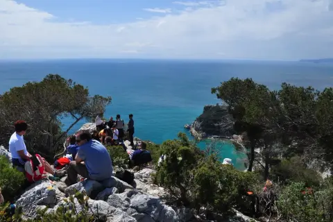 Gruppo di persone in pausa durante un trekking a Finale Ligure, con vista sul mare azzurro e scogliere.