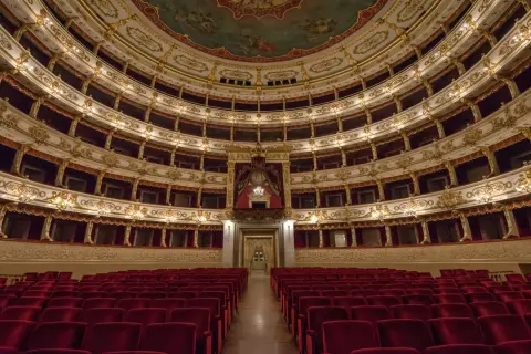 Interno di un teatro storico con file di poltrone rosse e palchi dorati. Un luogo da scoprire tra le cose da vedere a Parma gratis.