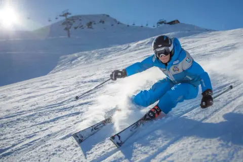 Sciatore in azione su una pista innevata, tipica delle località sciistiche Piemonte, con sole splendente e skilift sullo sfondo.