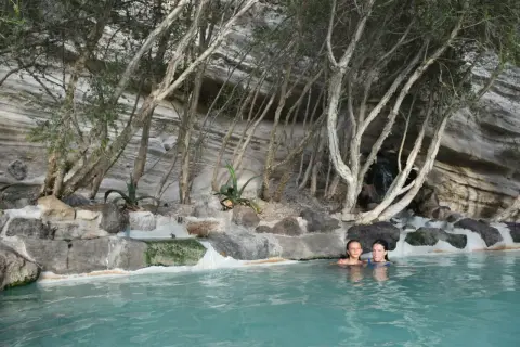 Due bambine si godono le terme libere di Ischia, immerse in acque turchesi tra rocce e vegetazione rigogliosa.