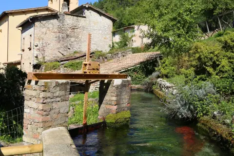Un canale d'acqua cristallina attraversa un borgo antico, ricordando la Venezia dell'Umbria. Edifici in pietra e vegetazione rigogliosa incorniciano questo scorcio pittoresco.