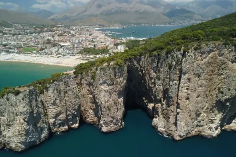 La leggenda della Montagna Spaccata a Gaeta: imponenti scogliere rocciose si tuffano nel mare blu, con la città sullo sfondo.
