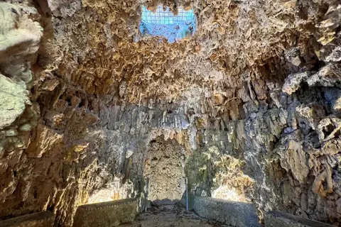 Interno di una grotta con stalattiti e stalagmiti, illuminata da una luce soffusa che filtra da un'apertura in alto. Sembra il ventre del **colosso dell'Appennino**.