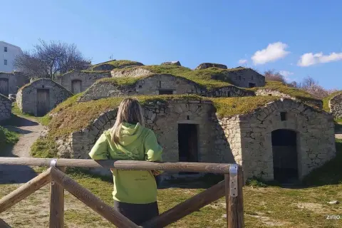 Pietragalla cosa vedere: antiche case-grotta scavate nella collina, con una donna che le osserva. Un luogo suggestivo da esplorare.