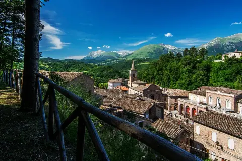 Borgo pittoresco nei Monti Sibillini, cosa vedere: tetti in cotto, campanile e montagne verdi.
