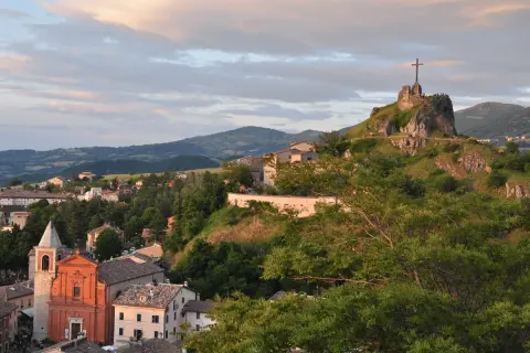 Panoramica di Pennabilli, Rimini, con la chiesa e la rocca con la croce che domina il paesaggio collinare al tramonto.