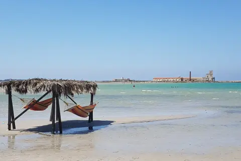 Amache colorate sotto un tetto di paglia, con il mare turchese e antichi edifici all'orizzonte. Un angolo di paradiso a San Teodoro, spiaggia rosa.