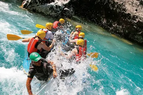 Un gruppo di persone si diverte con il rafting in Emilia Romagna, pagaiando tra spruzzi d'acqua cristallina e rocce.
