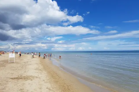 Giornata di sole e nuvole sul mare di Riccione. Bambini giocano sulla battigia mentre adulti passeggiano sulla sabbia dorata.