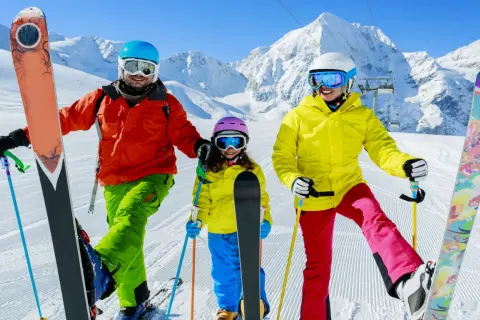 Famiglia felice sulle piste innevate, pronta dove imparare a sciare. Montagne maestose e cielo azzurro fanno da sfondo a questa avventura.