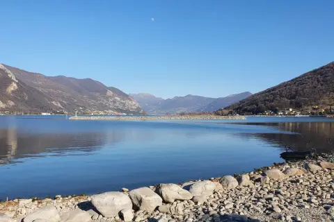 Calm lake with mountains in the background and a rocky shore in the foreground.