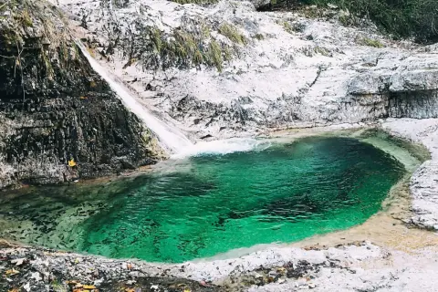 Cascata e pozza smeraldo nella valle del Mis, con rocce bianche e vegetazione.
