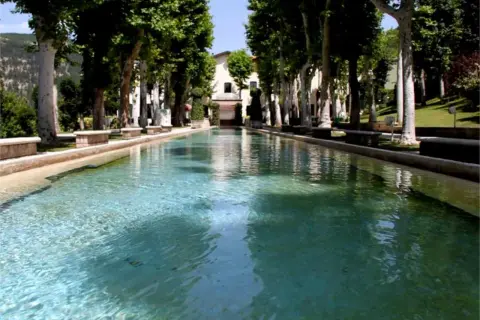 Vasca d'acqua cristallina con alberi secolari e un edificio sullo sfondo, un'oasi di pace a Caramanico Terme.