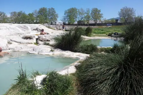Persone rilassate nelle piscine naturali di acqua termale, un'oasi di pace tra rocce bianche e vegetazione rigogliosa, un vero paradiso per chi cerca le piscine carletti.