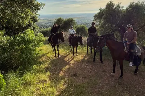 Quattro persone godono di una passeggiata a cavallo toscana, con vista panoramica sulla campagna.