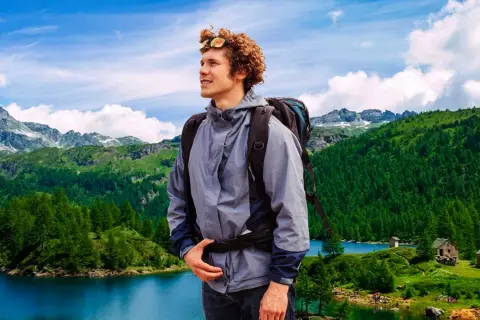 Giovane escursionista con zaino ammira un paesaggio alpino con laghi e boschi nel Piemonte.