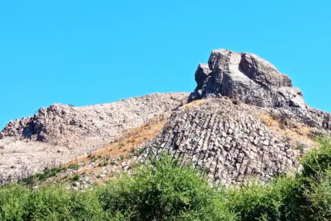 Rocciosa cresta nella Planargia, Sardegna, sotto un cielo azzurro. Vegetazione verde rigogliosa in primo piano.