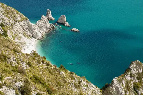 Scogliere bianche e mare turchese in una splendida località sulla riviera del Conero. Una piccola spiaggia nascosta e faraglioni emergono dall'acqua cristallina.