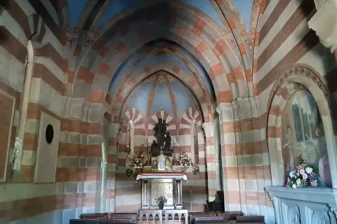 Interno di una cappella con volte a crociera a strisce rosse e bianche. Al centro, un altare con statue e fiori. Un esempio di cosa vedere a Berceto.