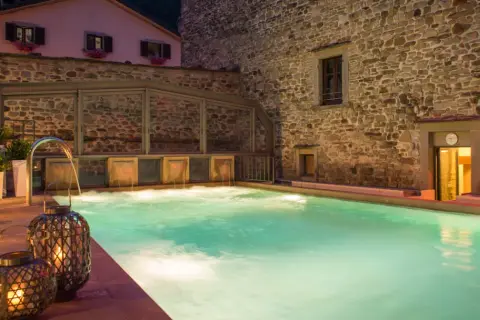 Piscina termale illuminata da lanterne, con cascate d'acqua e un edificio in pietra. Un'oasi di relax che ricorda le terme della Riviera Romagnola.
