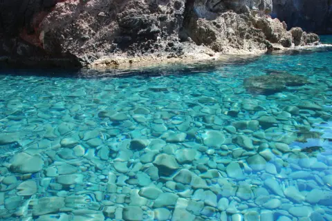 Acque cristalline del mare di Capraia, con fondale roccioso e ciottoli visibili sotto la superficie turchese.