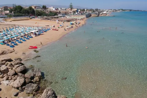 Una spiaggia affollata con lettini e ombrelloni, bagnanti in acqua e due kayak rossi sulla sabbia. Il noto mare cristallino invita a un tuffo.