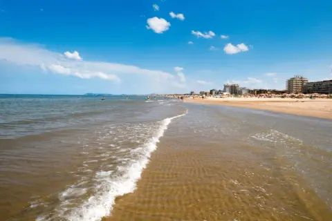 Onda leggera sulla sabbia dorata, con bagnanti e hotel sullo sfondo. Un classico giorno di **mare Emilia Romagna**.