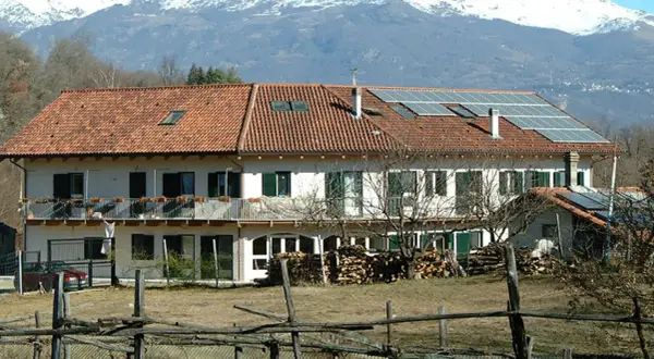 Edificio con pannelli solari, forse parte della comunità Damanhur, con montagne innevate sullo sfondo.
