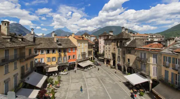 Piazza colorata con montagne sullo sfondo, un assaggio di dove si trova Domodossola.
