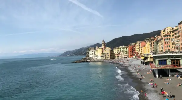 Un angolo di **mare vicino Milano**, con case colorate affacciate su una spiaggia di ciottoli e gente che prende il sole.