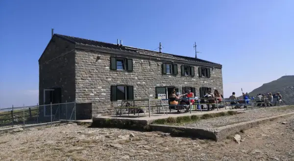 Rifugio in pietra con persone sedute ai tavoli all'esterno, un luogo ideale per una pausa durante un'escursione nei rifugi Emilia Romagna.