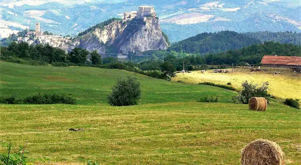 Colline romagnole dove andare: un borgo arroccato su uno sperone roccioso, campi verdi e balle di fieno.