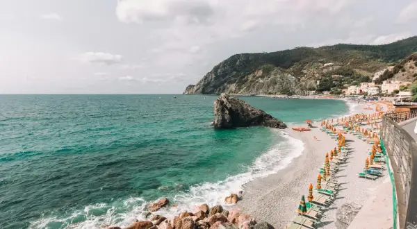 Spiagge libere Liguria: mare turchese, scogli imponenti e file di ombrelloni colorati su una spiaggia di ciottoli.