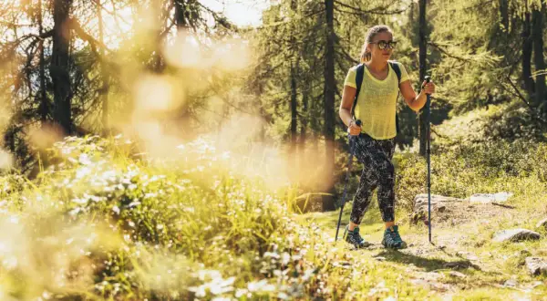 Giovane donna con bastoncini da trekking si gode le sue passeggiate Trentino in un bosco soleggiato.
