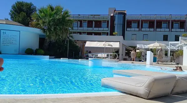 Piscina azzurra e lettini prendisole in un resort, con un edificio moderno sullo sfondo. Un'oasi di benessere e relax, perfetta per godersi le terme Viterbo Salus.