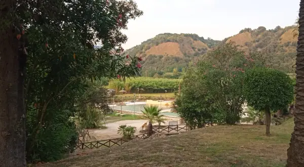 Un angolo di pace ad Agnano, dove si trova un complesso con piscine e vegetazione lussureggiante, incorniciato da colline verdi.
