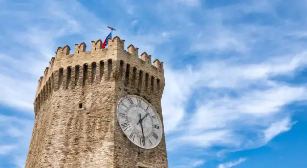 Torre dell'orologio a Gualtieri, con bandiera tricolore e cielo azzurro.