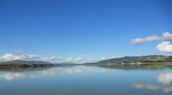 Lago calmo con riflessi di colline verdi e cielo azzurro. Un'ottima meta per scoprire cosa vedere vicino Matera.