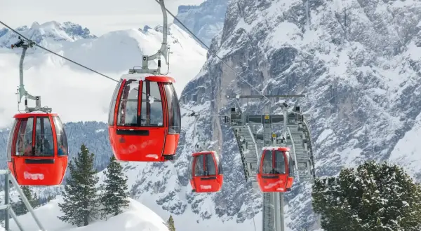 Cabine rosse su un impianto di risalita in Trentino, perfette per esplorare le località sciistiche economiche. Montagne innevate e pini sullo sfondo.