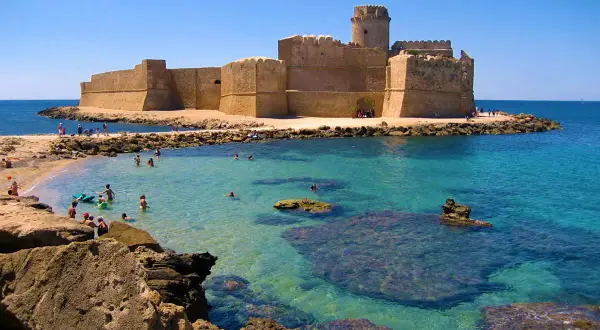 Castello Aragonese su una delle migliori spiagge calabria, con acque cristalline e bagnanti che si godono il sole.